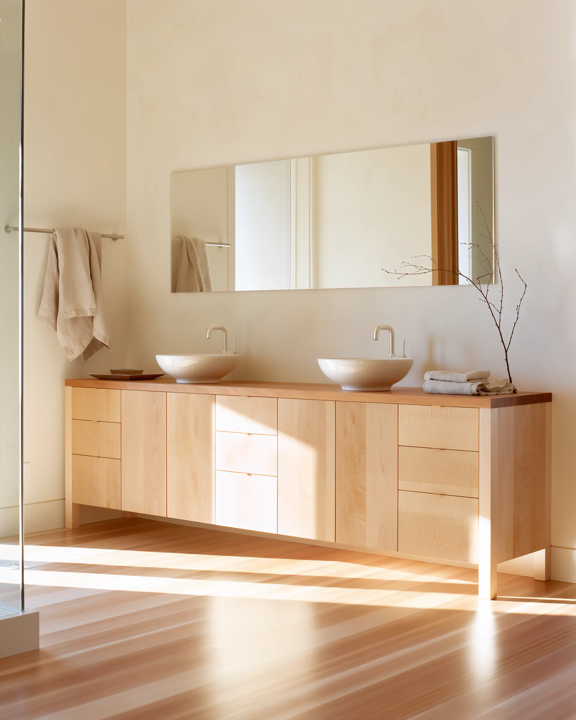 Long pale wood double vanity with fine drawers and a full-width mirror in a bright bathroom