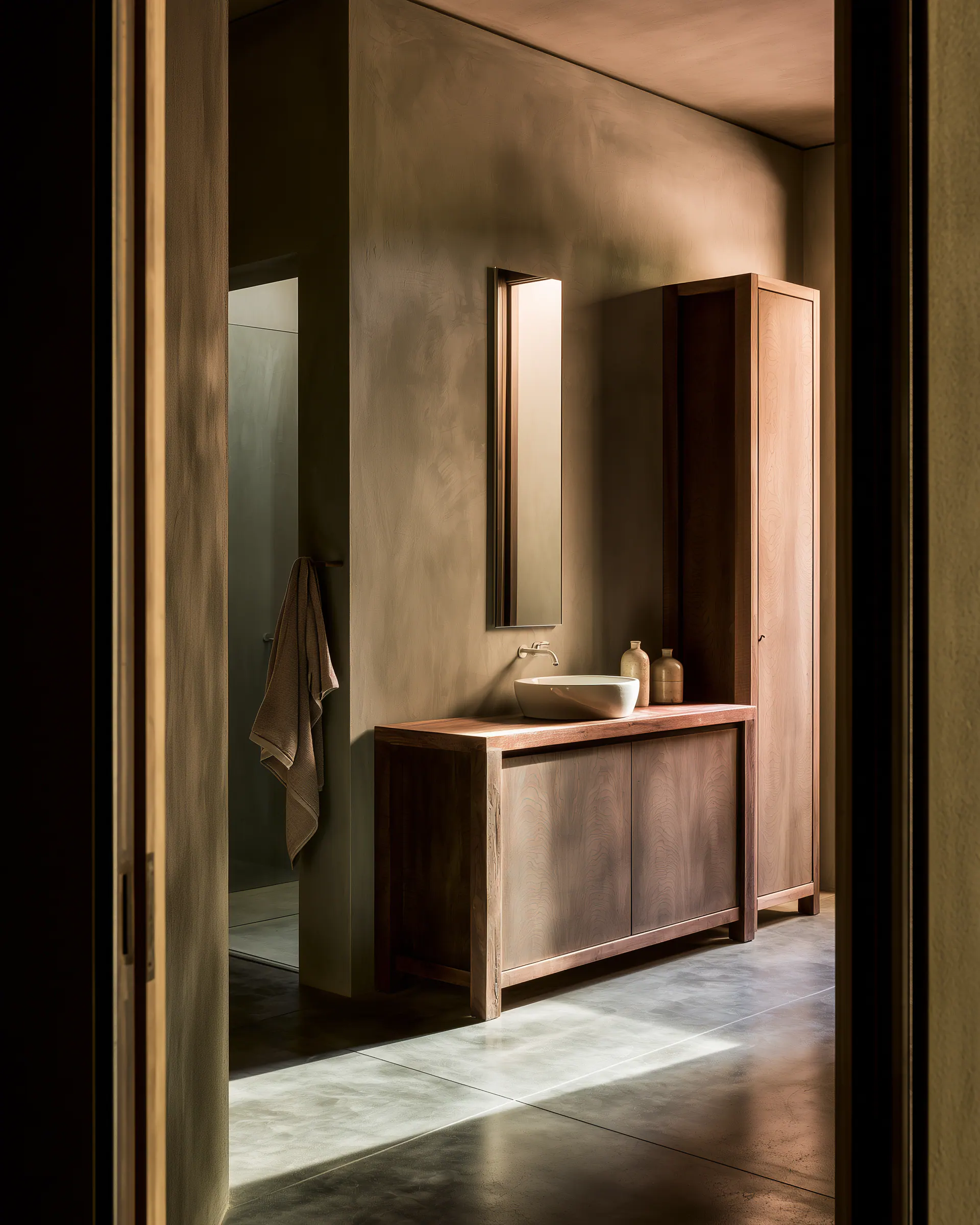 Dark wood freestanding vanity and tall cabinet viewed from a calm bathroom doorway