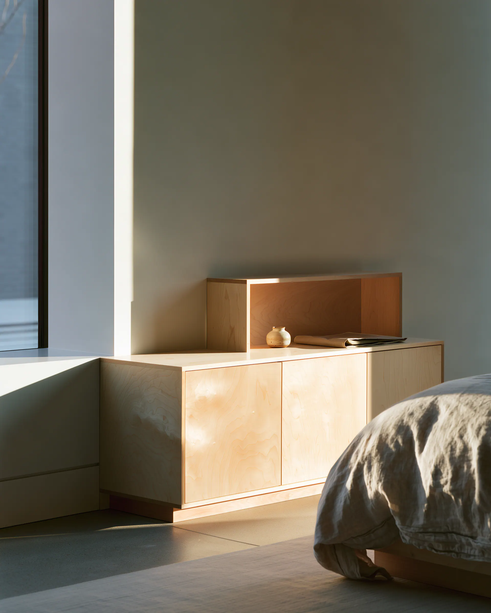 Compact light wood bedroom sideboard arranged beside a linen bed in soft morning light