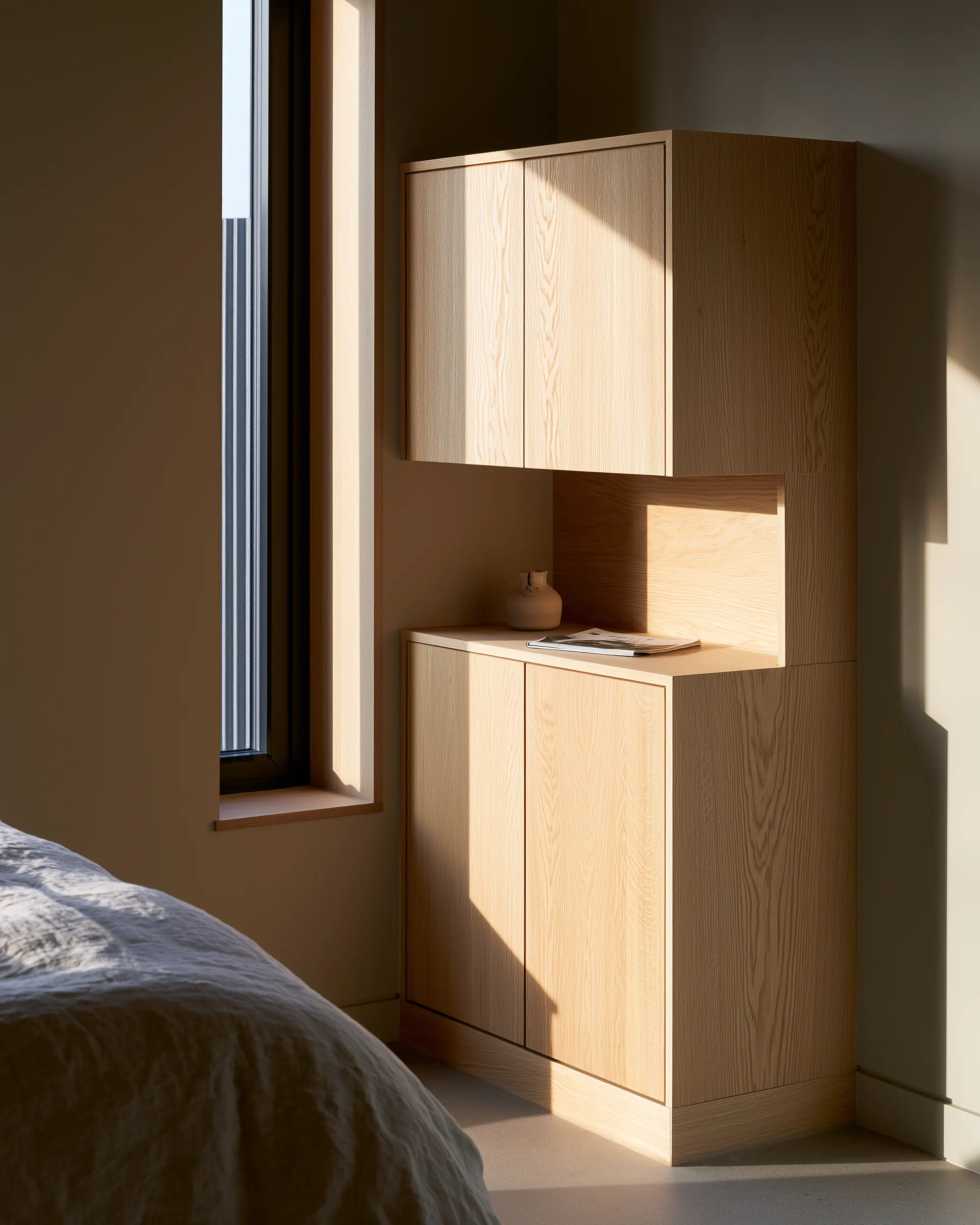 Stacked pale wood bedroom cabinets fitted around a narrow window and recessed writing surface