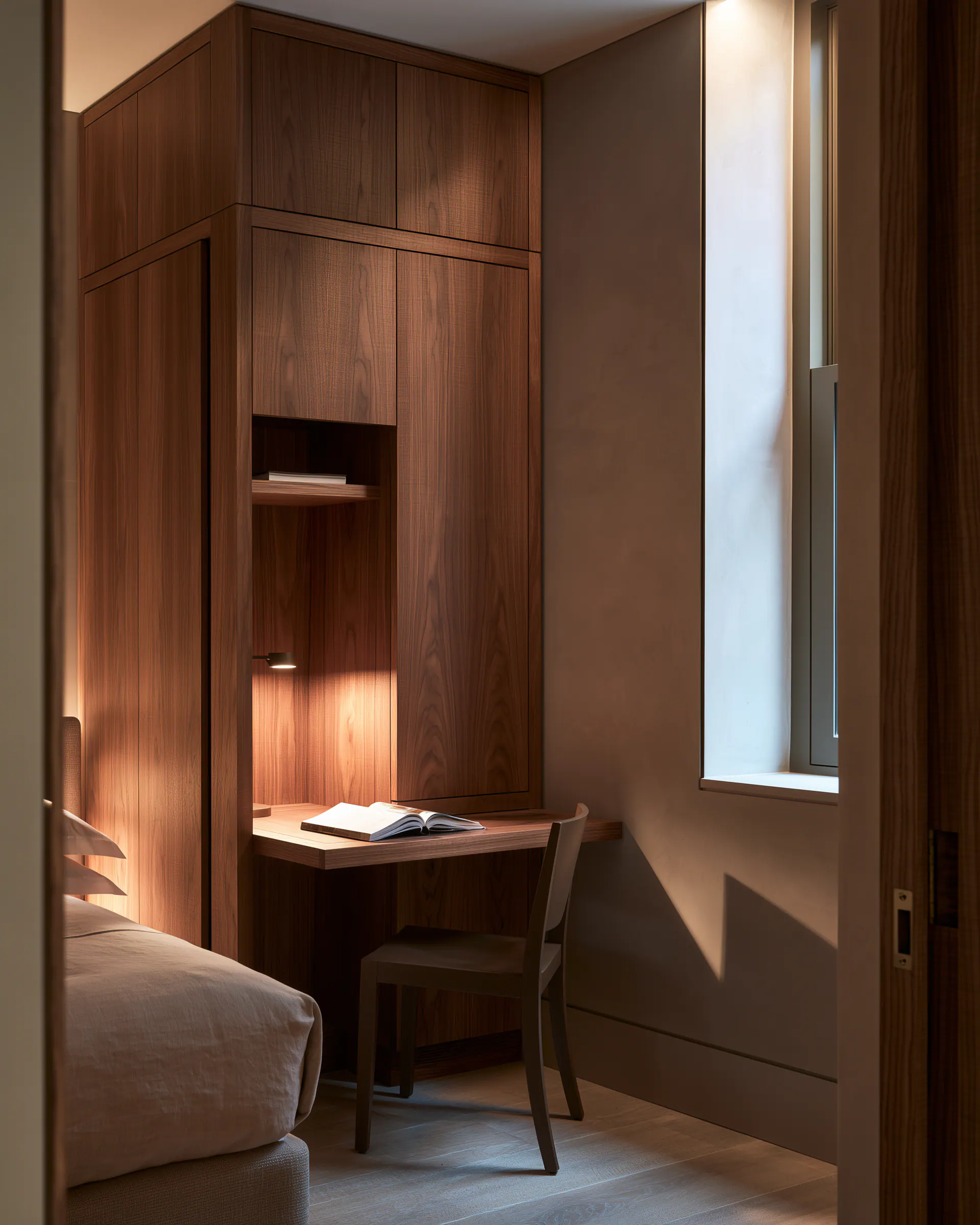 Dark wood bedroom storage wall with an integrated desk beside a softly dressed bed